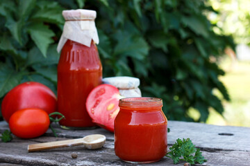 Homemade tomato sauce against a wooden table next to fresh tomatoes and herbs. Summer logging day at the dacha