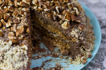 Delicious homemade cake with meringue, peanuts and walnuts on a light background. Sliced cake on a blue plate. Concept of natural homemade baking