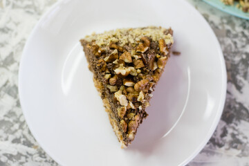 Delicious homemade cake with meringue, peanuts and walnuts on a light background. Appetizing piece of cake on a white plate close-up. Concept of natural homemade baking