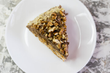 Delicious homemade cake with meringue, peanuts and walnuts on a light background. Appetizing piece of cake on a white plate close-up. Concept of natural homemade baking