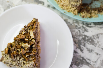 Delicious homemade cake with meringue, peanuts and walnuts on a light background. Appetizing piece of cake on a white plate close-up. Concept of natural homemade baking