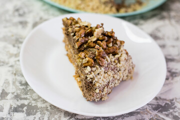 Delicious homemade cake with meringue, peanuts and walnuts on a light background. Appetizing piece of cake on a white plate close-up. Concept of natural homemade baking