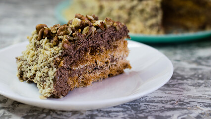 Delicious homemade cake with meringue, peanuts and walnuts on a light background. Appetizing piece of cake on a white plate close-up. Concept of natural homemade baking