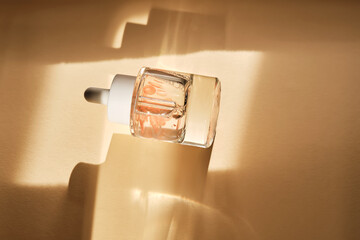 A bottle of luxury serum with petals on a beige background.