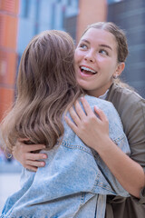  Two happy Caucasian women hugging and smiling outdoors, expressing joy and friendship. Emotional reunion, connection, and positive feelings in a modern urban setting with warm natural light. 