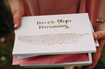 Young bridesmaid holding white wooden card box with text (Never stop dreaming) and feather print....
