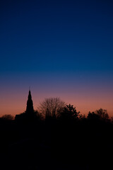Fototapeta premium Sunset at the golden hour with the silhouette of the Christuskirche and a leafless tree in Ratingen Homberg with orange and blue sky