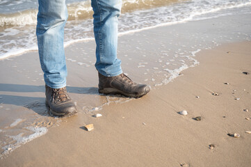 legs of a man in blue jeans, standing on a beach in hiking boots