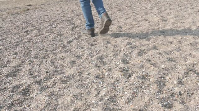 blue jeans of a man walking with hiking boots across a gravel beach, Vejle, Denmark, March 23, 2025

