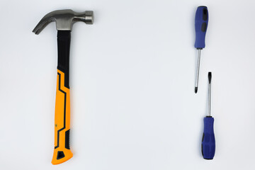 A hammer with an iron base and a yellow and black handle lies on the left, on the right there are screwdrivers on a white background with space for text in the center. The concept of repair, hammering