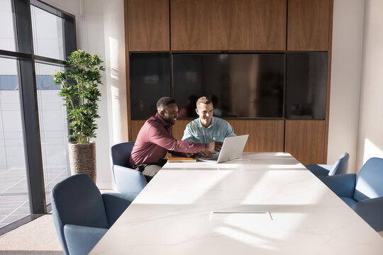 Multiethnic male workers using laptop met in contemporary meeting room. Manager consulting client, explain contract details, showing online presentation, share company services or business strategy