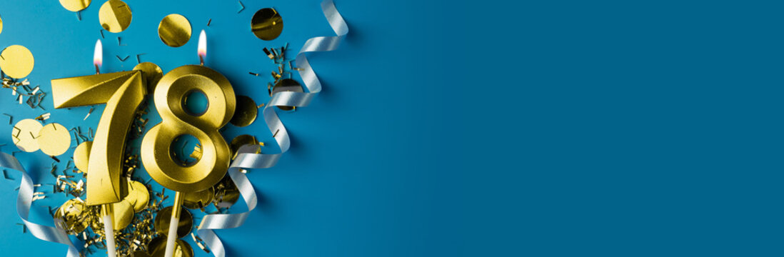 78 years celebration. Gold burning candles of number seventy-eight on blue background with confetti, copy space.