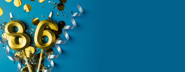 86 years celebration. Gold burning candles of number eighty-six on blue background with confetti,...