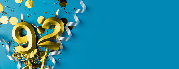 92 years celebration. Gold burning candles of number ninety-two on blue background with confetti,...