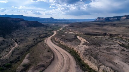 Stunning aerial view of winding dirt road through arid landscape and rugged mountains under a beautiful sky : Generative AI