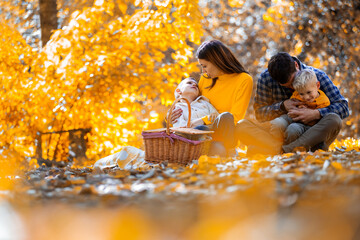 Loving family with two young sons enjoying a cozy autumn picnic in the park. They are smiling and hugging each other.