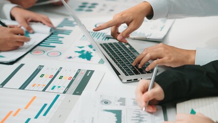 A team actively engaged in a business meeting focused on data analysis, utilizing a laptop and various documents to strategize and collaborate effectively in a modern office. SACTR