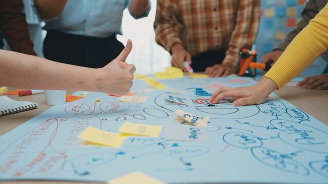 A dynamic workshop scene showcasing multiple hands engaged in writing and planning on a large paper with sticky notes, highlighting teamwork and creative thinking. SACTR