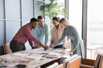 Multinational teammates professionals reviewing data with charts and graphs, take part in brainstorm session, generating ideas, sharing solutions during briefing or seminar event in corporate office