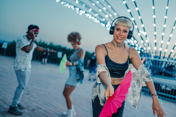 Young woman listening to music with headphones and dancing with a fan at a summer music festival