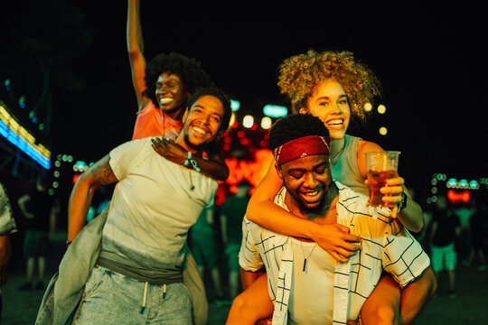 Friends having fun piggybacking at music festival at night