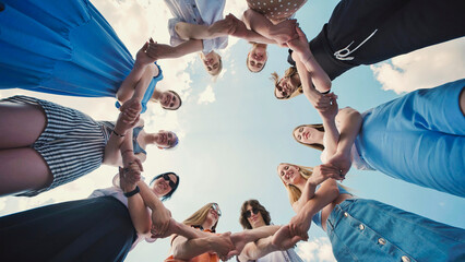 Group of school friends forming a circle, holding hands and gazing down at the camera, representing...
