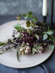 Elegant arrangement of dark flowers and greenery on a simple plate setting with soft lighting : Generative AI