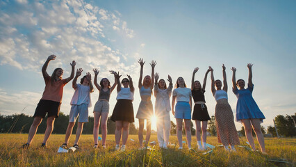 Group of happy students waving goodbye at sunset in a field, celebrating the end of school