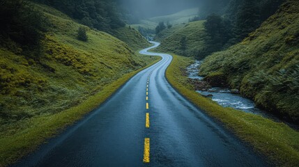 Serpentine asphalt road traversing lush green hills on a misty morning