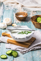 Greek tzatziki in a handmade white earthenware bowl with cucumber and garlic on a rustic wooden background