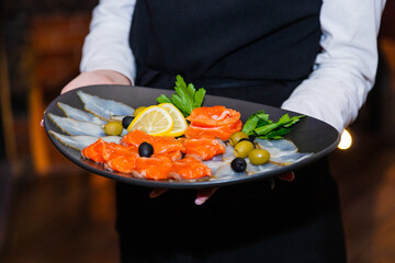 Sliced two varieties of fish with herbs in a plate in the hands of the waiter. close-up