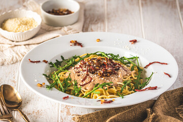 Spaghetti with chestnut sauce and crispy ham topping and arugula leaves on white wooden background