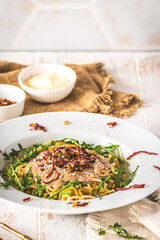 Spaghetti with chestnut sauce and crispy ham topping and arugula leaves on white wooden background