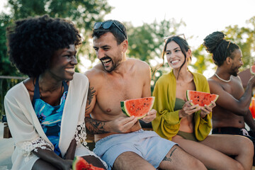 Happy friends eating watermelon by the pool during summer vacation