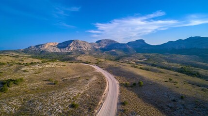 Fototapeta premium A scenic winding dirt road leading through a rugged landscape with mountains in the background : Generative AI