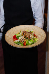 Salad with meat and nuts on a plate in the hands of the waiter