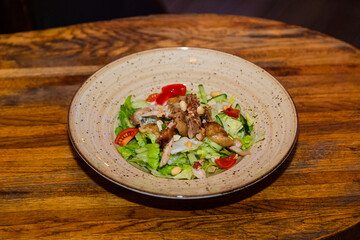 Salad with meat and nuts on a plate on a wooden table.Delicious food. general plan from above
