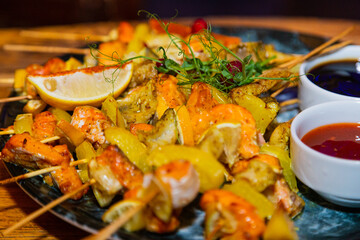 Shish kebab from seafood and red fish on wooden skewers on a plate with sauces on a wooden table. close-up of delicious food
