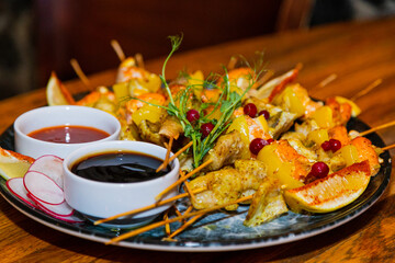 Shish kebab from seafood and red fish on wooden skewers on a plate with sauces on a wooden table. close-up of delicious food. food in the restaurant