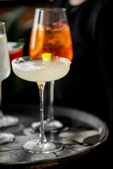 A tray of assorted cocktails, including a margarita with a salted rim and lemon garnish, and a tall orange drink, showcasing elegance and diversity in drink presentation.