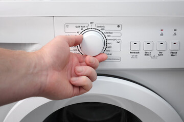 A man's hand sets the automatic washing program switch on the washing machine panel. Saving water...