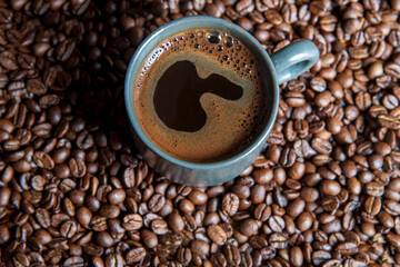 A cup of coffee with roasted coffee beans.