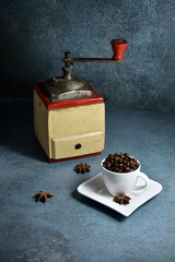Vintage coffee grinder and cup full of coffee beans.