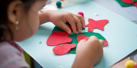 Child's hands arranging red and green felt shapes on light-blue surface, creating a craft project.  Focus on creative process and childhood activity