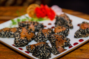 Grilled red fish meat with sesame seeds. A plate with fish and ginger on a wooden table in a restaurant. close-up of meat and sesame