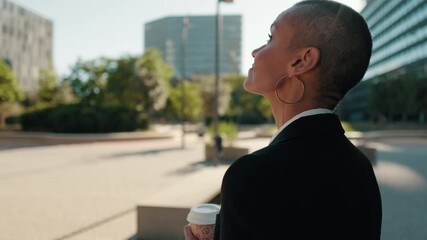 Businesswoman takes a moment to look at the city view. She holds a coffee cup and smiles as she observes the scenery.