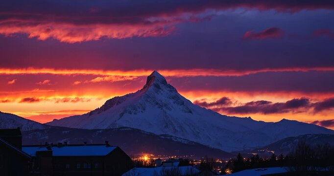 Stunning winter evening scene of the mountain, highlighting the peaks lit by a vibrant sunset. The sky is awash with warm hues in the snowy surroundings.