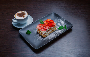 Appetizing dessert on a plate with fresh strawberries and a cup of cappuccino
