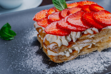 Appetizing dessert of strawberries and puff pastry with cream on a plate. mint leaves.close up