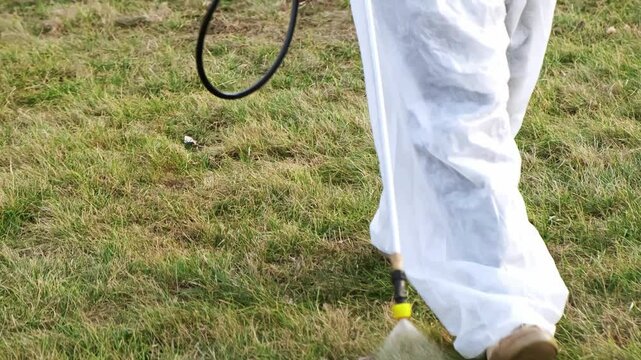 A man is spraying chemicals the lawn for weed control and from insect parasites using poison sprayer. Weedkiller. A gardener in personal protective suit equipment. High quality 4k footage.